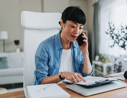 A woman talks on the phone while reading a document. 
