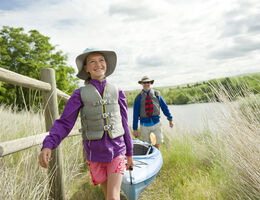 A man and a girl carry a kayak away from the water.