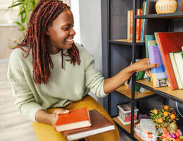 A woman organizes books on a shelf.