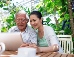 An older man uses a laptop as a younger woman looks on, smiling.