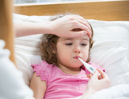 A woman feels a young girl's forehead and checks a thermometer.